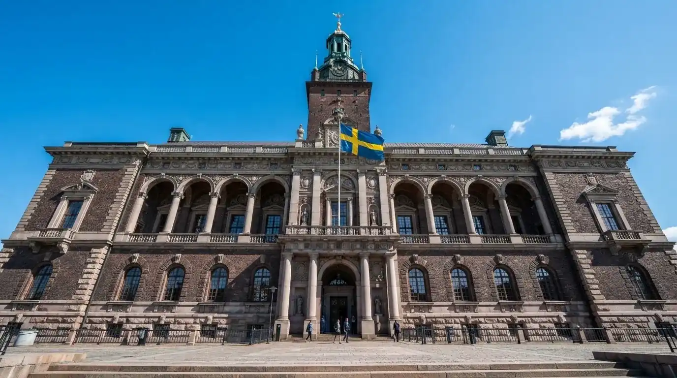Ett gammalt stadshus i sten fotograferat underifrån mot en klarblå himmel, med den svenska flaggan som fladdrar ovanför entrén.